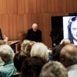 Dr Samuel Kassow speaking to audience with slide image of Josima Feldschuh in background.